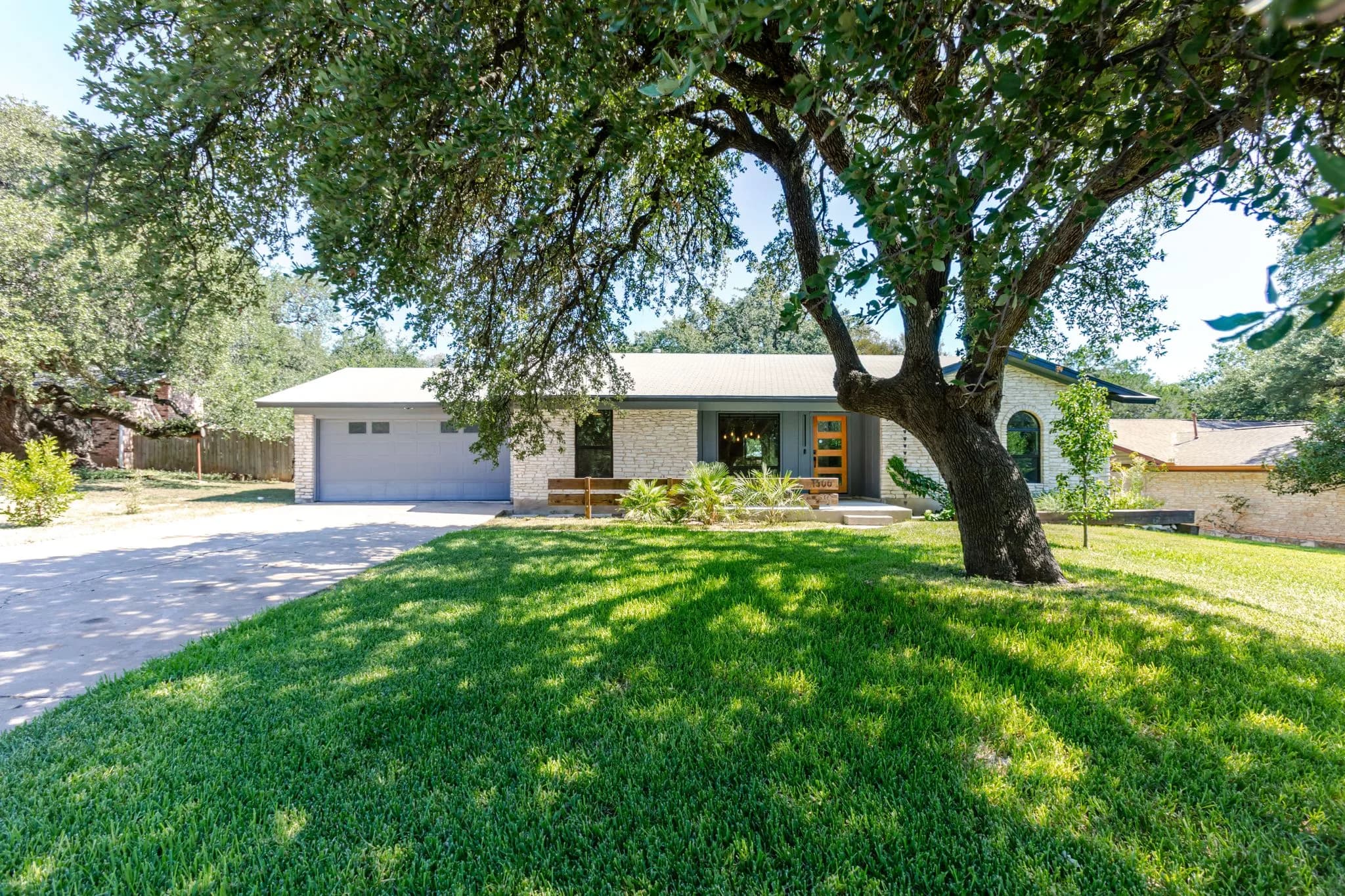 Single story ranch home behind a green lawn and a large live oak